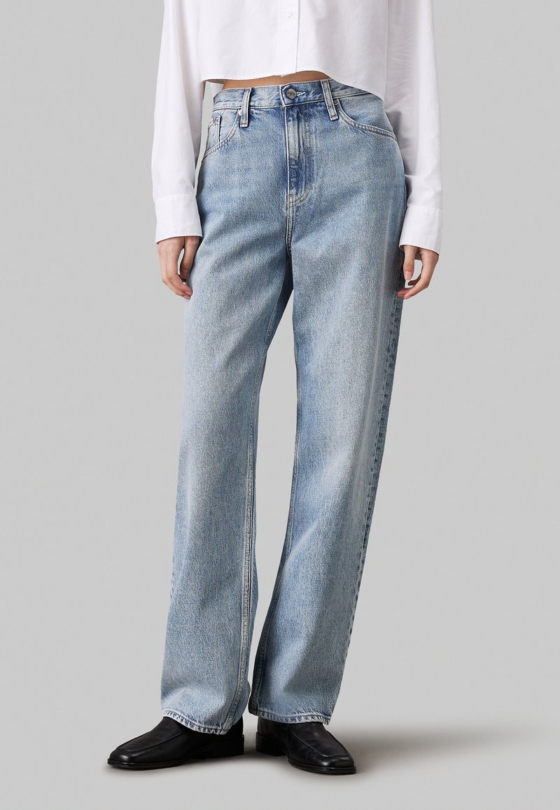 Jeans de tiro alto en denim, de pierna ancha y color azul claro, con bolsillos frontales y un ligero desgaste. Combinados con botas negras de tobillo.