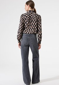 Blouse à manches longues avec un motif ikat beige et noir, associée à un jean en denim foncé à taille haute et jambes larges. Texture douce avec une coupe décontractée.