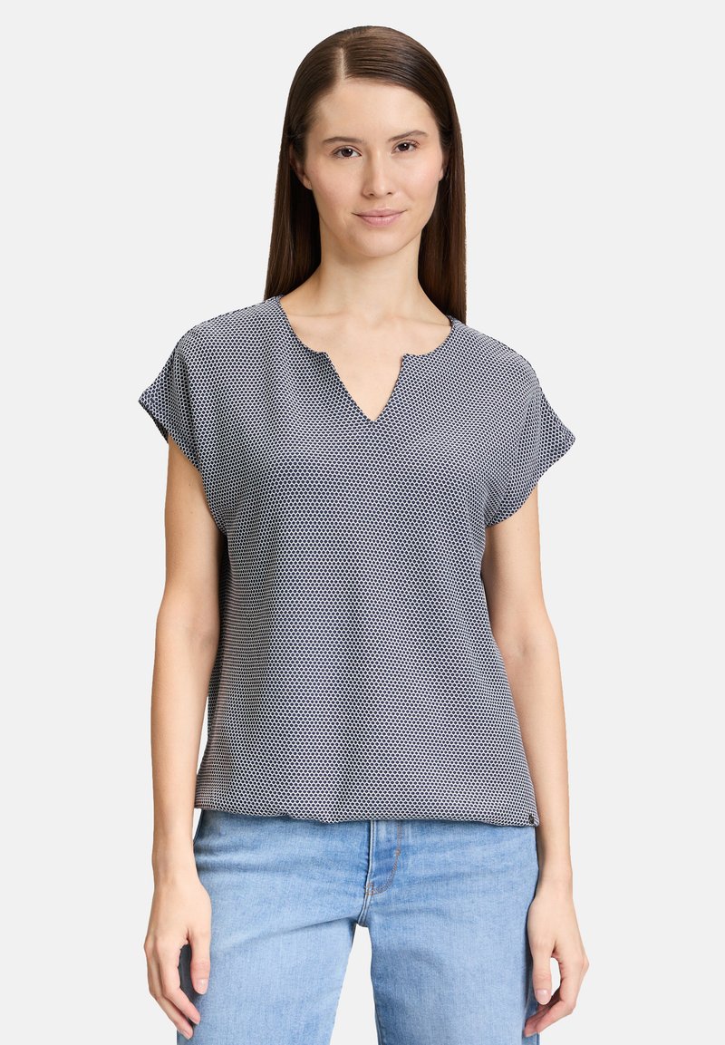 Top a manica corta di colore blu navy con pois bianchi, caratterizzato da un collo a V e una vestibilità rilassata. Tessuto leggero con una consistenza liscia.