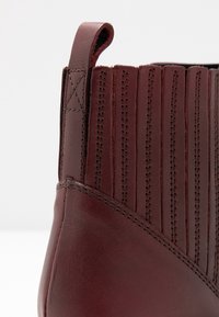Primer plano del tacón de una bota de cuero marrón oscuro con una lengüeta y paneles elásticos laterales verticales cosidos con dobles costuras.