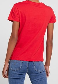 Rød bomulds t-shirt med korte ærmer og rund halsudskæring, båret med blå denim jeans med karakteristiske baglomme og syninger.
