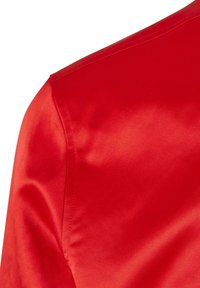 Gros plan sur un tissu satin rouge montrant la zone de l'épaule et du haut de la manche avec des détails de couture visibles.