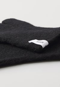 Guantes de lana negra con una textura suave, que presentan una etiqueta en un puño. El diseño es simple y estructurado, destacando la calidez y el confort.