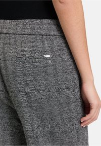 Grijze broek met visgraatpatroon, voorzien van een achterzak en een klein merkteken. De stof lijkt gestructureerd en geweven. Gepersonaliseerde pasvorm, gezien vanuit de zijkant.