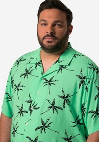 Zelená košile s krátkým rukávem a černým potiskem palmových listů, knoflíkové zapínání, límcový design, lehká tkanina a volný střih.