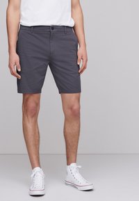 Shorts gris en tissu léger, dotés d'une fermeture à boutons, de passants pour ceinture et d'un ourlet retroussé, associés à des baskets montantes blanches.