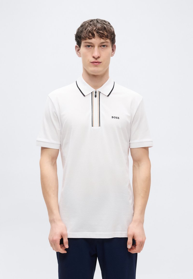 Λευκό πόλο μπλουζάκι με γιακά μισού φερμουάρ και μαύρες λεπτομέρειες. Διαθέτει κοντά μανίκια και μικρό λογότυπο BOSS στην αριστερή πλευρά. Λεπτή υφή.