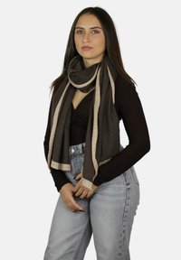 Sciarpa marrone con dettagli metallici dorati, texture morbida, drappeggiata elegantemente intorno al collo, abbinata a un top aderente e jeans chiari.