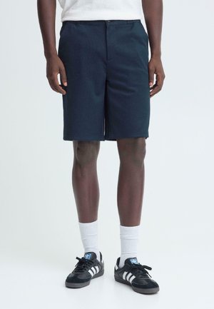 Marineblauwe korte broek gemaakt van lichtgewicht stof, met een losse pasvorm en zijzakken. Gecombineerd met zwarte sneakers en witte sportsokken.