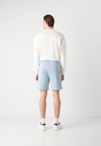 Shorts de un albastru deschis dintr-un material moale, având un buzunar la spate. Asortate cu un hanorac alb cu gât rotund și încălțăminte casual.