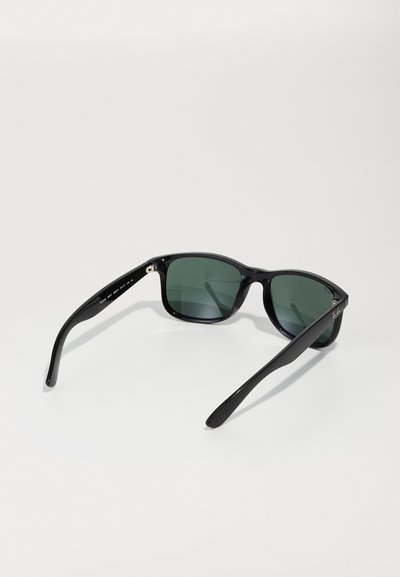 Lunettes de soleil noires avec verres verts, design rectangulaire, monture en plastique brillant et branches fines. Détail du logo près de la charnière.