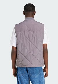 Ljust grått vadderat väst med hög krage, med slät textur och diamantmönster, bärs över en vit skjorta och blå jeans.