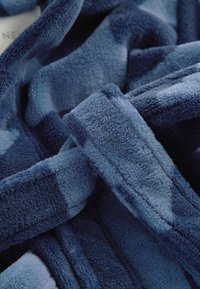 Blåt fleecestof med en blød, tekstureret overflade, der har en blanding af mørkere og lysere blå nuancer i et subtilt mønster.