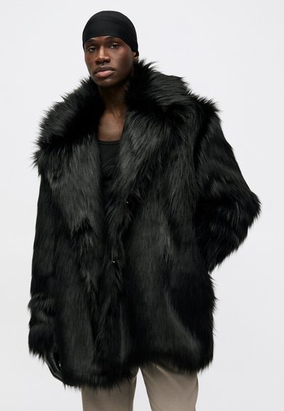 Černý kožich z umělé kožešiny s širokým límcem, dlouhými rukávy a texturovanou tkaninou. Má volný střih a zapínání na knoflík vpředu.