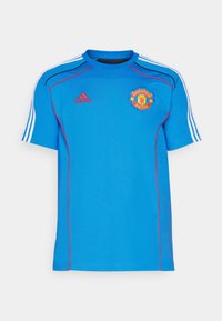Mėlyna trumpa rankovė sportinė marškinė, pagaminta iš medvilnės, su raudonais akcentais ir "Manchester United" logotipu priekyje, su baltais dryžiais ant pečių.