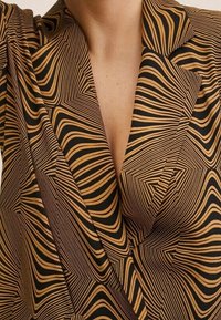 Brązowo-czarny marynarka w paski z geometrycznym falistym wzorem noszona przez osobę z widoczną linią szyi i obojczykiem.