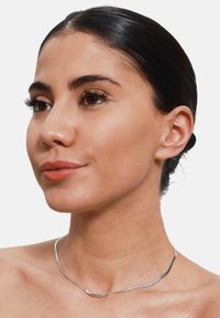 Silberne Choker-Halskette mit einem glatten, gewellten Design. Sie hat eine polierte Oberfläche und wirkt leicht, während sie auf einem nackten Hals ruht.