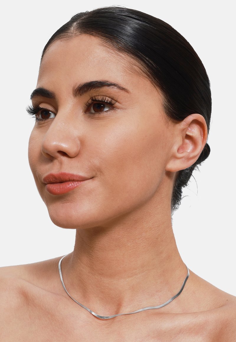 Sølv choker halskjede med et glatt, bølgete design. Har en polert overflate og fremstår lett, hvile på en naken nakke.