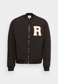 Svart bomberjacka med dragkedja fram, ribbstickade muddar och en broderad vit "R" på vänster bröstområde. Mjuk tyg, figursydd design.