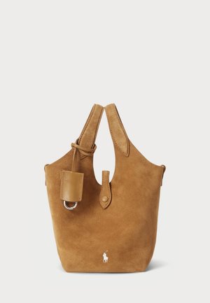 Wildleder-Tasche in Tan mit runder Form. Verfügt über ein Leder-Akzent, einen abnehmbaren Tragegurt und ein kleines Logo auf der Vorderseite. Minimalistisches Design.