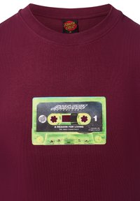 T-shirt bordeaux con grafica stampata di una cassetta verde con accenti neri e blu, etichettata "Santa Cruz" e "A Reason for Living."