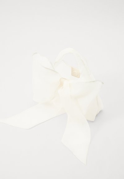 Bijela platnena torba s velikim detaljem mašne i dvjema kratkim ručkama. Tekstura je glatka, stvarajući mekan i lepršav izgled.