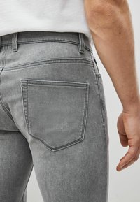 Jeans din denim gri cu un design ajustat, buzunare din spate cu cusături subtile și o textură netedă. Include bucle pentru curea la talie.