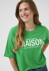 Zielona bawełniana koszulka z okrągłym dekoltem, krótkimi rękawami i białym nadrukiem z przodu, na którym widnieje tekst "MAISON" oraz "Art of Creation."