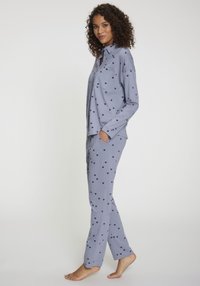 Ljusblå pyjamasset med små svarta hjärtan, innehållande en knapp-up skjorta med ficka och raka byxor. Mjukt tyg.