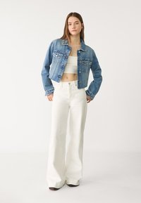 Denimska jakna v svetlo modri barvi, skrajšanega kroja z dvema žepoma na prsih. Kombinirana z belimi širokimi hlačami, izdelanimi iz teksturirane tkanine.