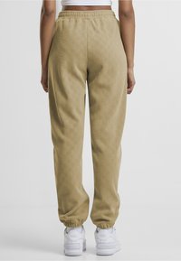 Beige rutete joggebukser med elastisk midjebånd og smalere ben, kombinert med hvite joggesko, som viser en teksturert stofffinish.