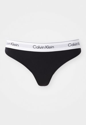 Black thong underwear made of smooth fabric. Features a white waistband with "Calvin Klein" logo printed in black. Classic design and minimal coverage.