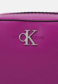 Fuksjowa torba z syntetycznej skóry z wytłoczonym logo "Calvin Klein Jeans" oraz srebrnymi detalami "CK", charakteryzująca się gładką fakturą.