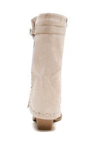 Botín de ante beige con una textura suave, cremallera expuesta y tachuelas decorativas plateadas a lo largo del costado, con un bajo tacón de madera.