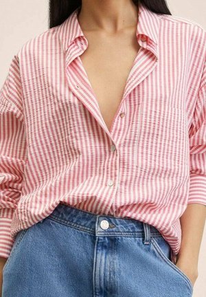 Femme portant une chemise à rayures verticales roses et blanches, boutonnée et rentrée dans un jean en denim bleu taille haute, la main dans la poche.