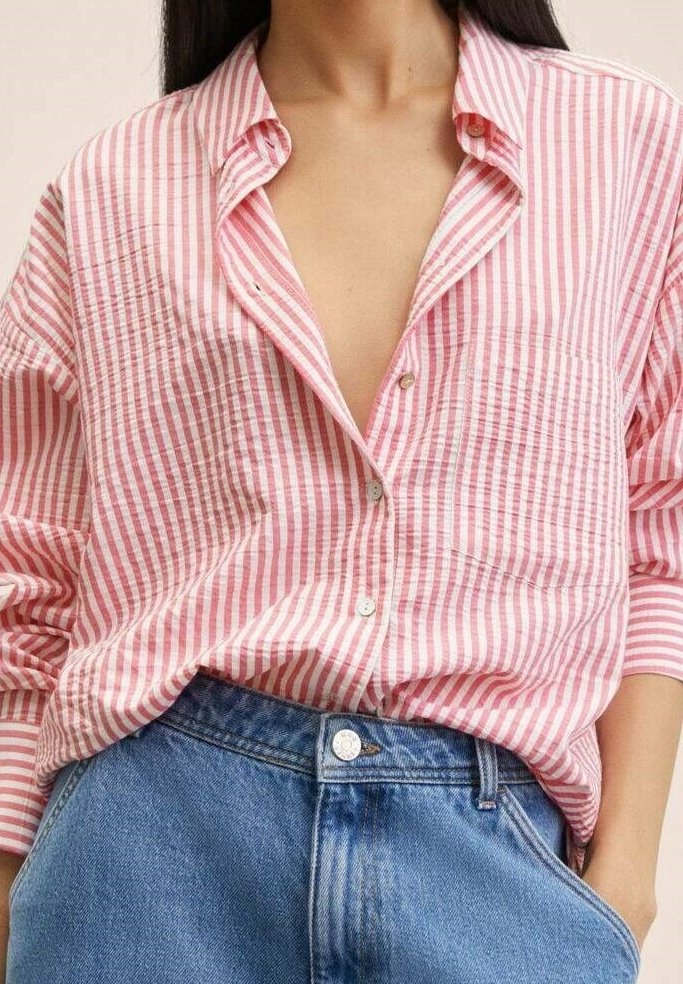 Femme portant une chemise à rayures verticales roses et blanches, boutonnée et rentrée dans un jean en denim bleu taille haute, la main dans la poche.