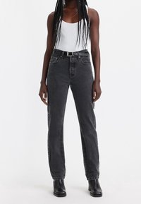 Jeans de denim negros de tiro alto con perneras rectas, que cuentan con detalles de hardware plateado y una tela texturizada. Incluye cinturón negro.