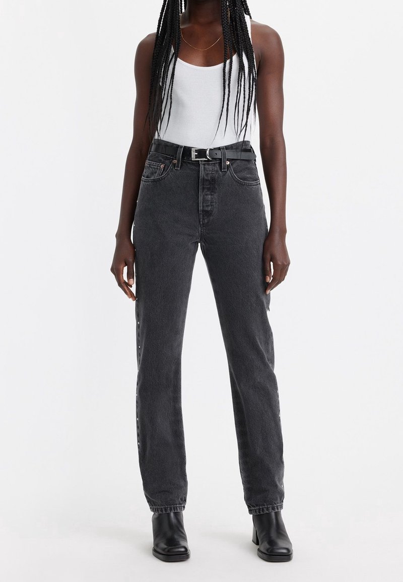 Jeans de denim negros de tiro alto con perneras rectas, que cuentan con detalles de hardware plateado y una tela texturizada. Incluye cinturón negro.