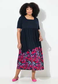 Marineblaues Kleid mit kurzen Ärmeln, quadratischem Ausschnitt und einem floralen Muster in Pink und Blau am Saum. Weicher Stoff, knöchellang, fließendes Design.