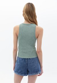 Grönribbad tanktop med rund halsringning, i kombination med högmidjade denimshorts. Tygmaterialet är slätt och åtsittande, vilket framhäver silhuetten.