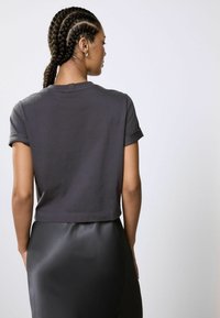 Dunkelgraues, kurz geschnittenes T-Shirt mit kurzen, aufgerollten Ärmeln, aus weichem Stoff, kombiniert mit einem glatten, schwarzen Rock für einen Kontrast in der Textur.
