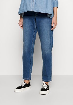 Osoba nosząca niebieskie dżinsy denim, czarno-białe casualowe sneakersy oraz jasnoniebieską koszulę jeansową z podwiniętymi rękawami.