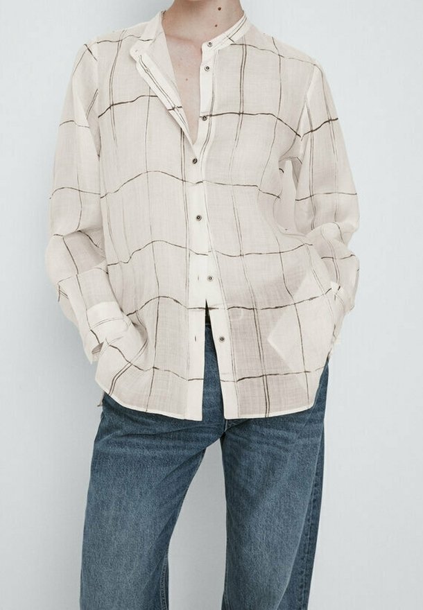 Lys beige skjorte med knapper, sort rutemønster, lange ærmer og mandarin-krave. Parret med blå denim jeans.