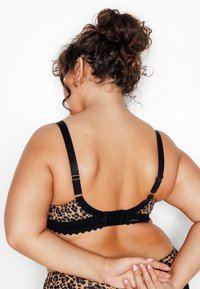Soutien-gorge à imprimé léopard avec bretelles réglables noires et fermeture à agrafes. Caractéristiques des bords festonnés et une texture douce pour le confort.