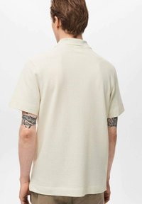 Șirt polo cu mânecă scurtă în nuanță off-white, cu textură ribbed. Dispune de un guler plat și este realizat dintr-un material ușor, destinat unei potriviri relaxate.