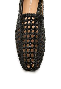 Mocasines tejidos negros con un diseño abierto, que presentan un patrón texturizado y una plantilla suave de color marrón claro.