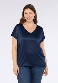 Yhden värinen, tummansinisestä satiinista valmistettu lyhythihainen V-pääntie paita. Mallissa on rento malli, jossa on hieman laskeutuneet olkapäät.