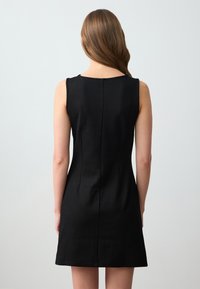 Vestito nero senza maniche con silhouette aderente, caratterizzato da un collo rotondo, tessuto morbido e una cucitura che corre lungo il centro della schiena.