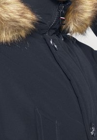 Černá parka bunda s kapucí lemovanou kožešinou, vybavená zapínáním na zip a knoflíky, texturovanou tkaninou a předními kapsami.