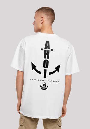 White cotton t-shirt featuring bold black graphics: "AHOI" with arrows and a sailor logo; relaxed fit and short sleeves.